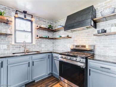 Kitchen featuring brick wall, stainless steel gas range, dark stone countertops, and sink
