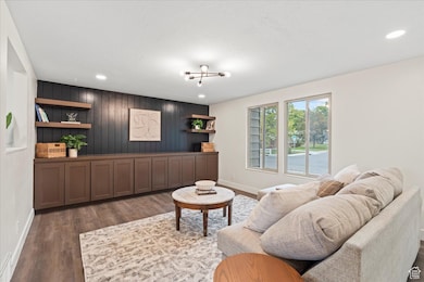 Living room with dark wood-style floors, wooden walls, and recessed lighting