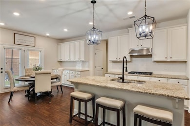 Kitchen with a chandelier, a sink, under cabinet range hood, white cabinets, and recessed lighting