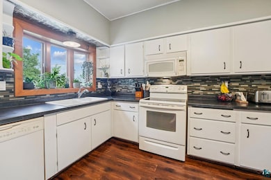 Kitchen with white appliances, tasteful backsplash, dark countertops, and crown molding