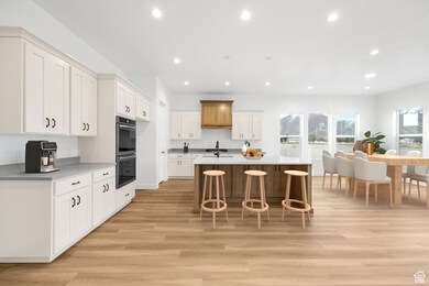 Kitchen featuring light wood-type flooring, an island with sink, a kitchen breakfast bar, recessed lighting, and white cabinetry