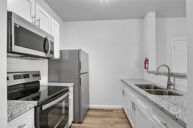 This kitchen features sleek, modern updates with stainless steel appliances, including a microwave, oven, and refrigerator. The space is enhanced by granite countertops and white cabinetry, providing a clean and contemporary look. A double-basin sink with a modern gooseneck faucet offers added convenience. The kitchen is well-lit with bright lighting, and the luxury vinyl plank adds a touch of warmth to the overall minimalist design. Ideal for those seeking a functional and stylish cooking space.