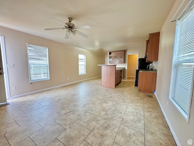 Kitchen with ceiling fan, black fridge, light tile patterned floors, and kitchen peninsula