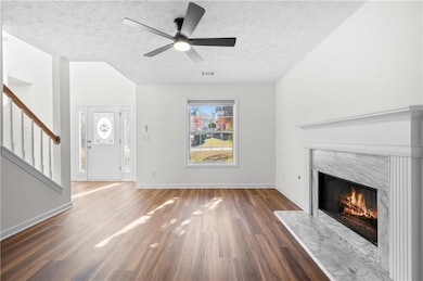 Unfurnished living room featuring stairway, a high end fireplace, a textured ceiling, dark wood-style flooring, and a ceiling fan