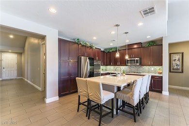 Kitchen featuring light countertops, a breakfast bar area, stainless steel appliances, a center island with sink, and pendant lighting