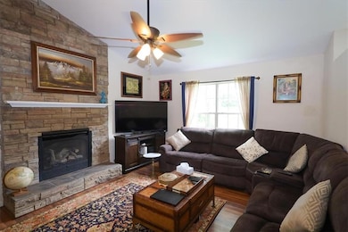 Living room with a ceiling fan, wood finished floors, lofted ceiling, and a stone fireplace