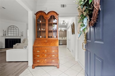 Foyer entrance featuring crown molding, a chandelier, light tile patterned flooring, and a fireplace