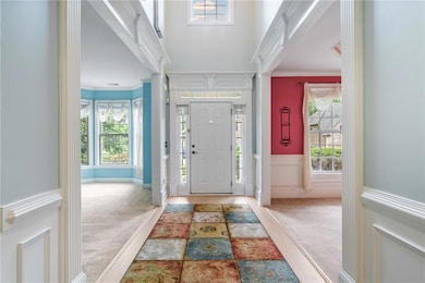 Carpeted foyer with ornamental molding, wainscoting, and a decorative wall