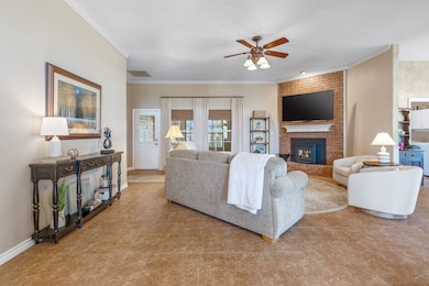 Living area with a brick fireplace, ceiling fan, and crown molding