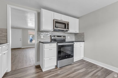Kitchen featuring stainless steel appliances, decorative backsplash, light wood finished floors, white cabinets, and dark countertops