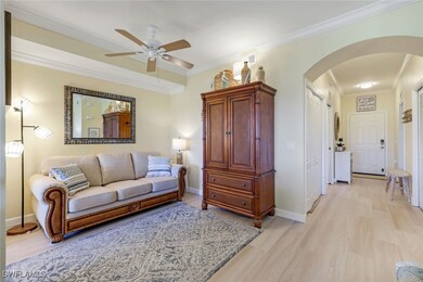 Living room with crown molding, light wood finished floors, baseboards, a ceiling fan, and arched walkways