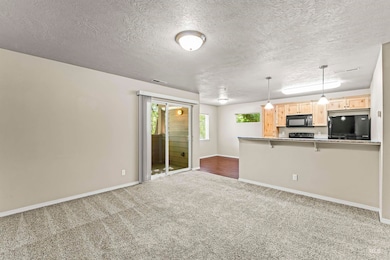 Kitchen with black microwave, refrigerator, light brown cabinets, carpet flooring, and a kitchen breakfast bar