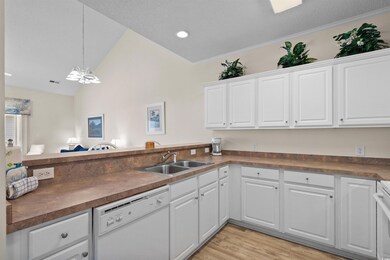 Kitchen with white dishwasher, dark countertops, white cabinetry, vaulted ceiling, and light wood finished floors