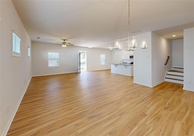 Unfurnished living room featuring ceiling fan with notable chandelier, light hardwood / wood-style floors, and sink