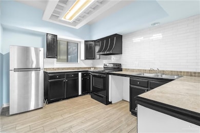 Kitchen with black electric range oven, a sink, dark cabinetry, freestanding refrigerator, and exhaust hood