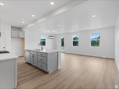 Kitchen with gray cabinetry, recessed lighting, a kitchen island with sink, light wood-style floors, and a chandelier