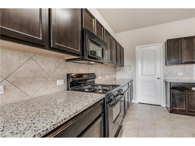 Kitchen with dark brown cabinets, black appliances, and decorative backsplash