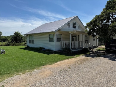 View of front of property featuring a porch, a front yard, a metal roof, and driveway