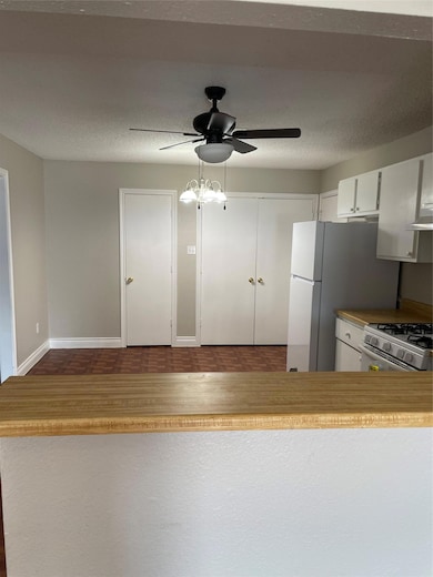 Kitchen featuring white cabinets, range, light countertops, a textured ceiling, and exhaust hood