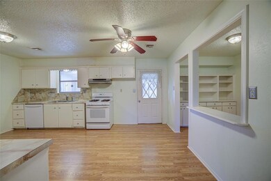 Kitchen featuring white appliances, a textured ceiling, a sink, light wood-style floors, and white cabinetry