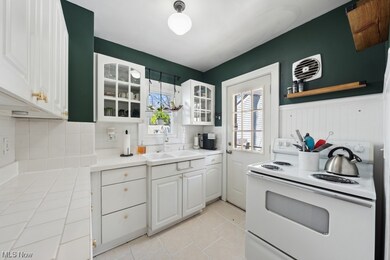 Kitchen with white cabinets, backsplash, light tile flooring, electric stove, and sink