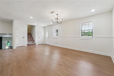 Unfurnished living room with stairway, a chandelier, light wood-style flooring, plenty of natural light, and recessed lighting