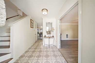 This photo shows a bright, welcoming entryway with patterned tile flooring. To the left, there's a staircase with wooden steps. Straight ahead, a hallway leads to a dining area.
