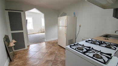Kitchen with white appliances, arched walkways, exhaust hood, light colored carpet, and light tile patterned floors
