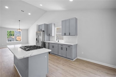 Kitchen with stainless steel appliances, a sink, gray cabinetry, vaulted ceiling, and light wood finished floors