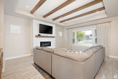 Living room featuring a tray ceiling, a large fireplace, light wood finished floors, beamed ceiling, and recessed lighting