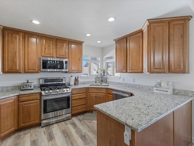 Kitchen with light stone countertops, appliances with stainless steel finishes, brown cabinets, and recessed lighting