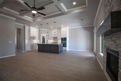 Kitchen featuring decorative light fixtures, a fireplace, stainless steel oven, coffered ceiling, and an island with sink