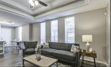 Living room with dark wood-type flooring, a tray ceiling, ceiling fan, and baseboards