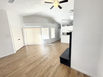 Unfurnished living room featuring light wood finished floors, vaulted ceiling, a textured ceiling, and ceiling fan