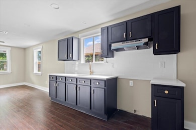 Kitchen with extractor fan, a sink, dark wood-style flooring, light countertops, and backsplash