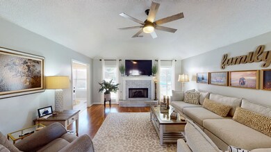 Living area with vaulted ceiling, ceiling fan, wood finished floors, a fireplace, and a textured ceiling