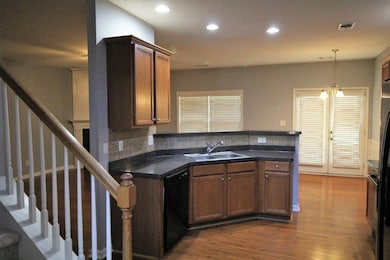 Kitchen with a peninsula, dark wood finished floors, decorative light fixtures, brown cabinets, and black appliances