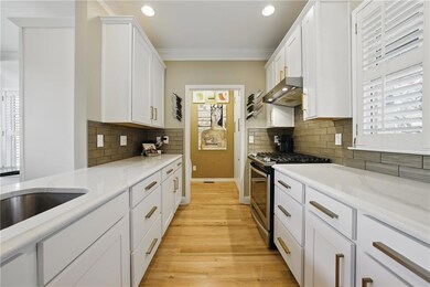 Kitchen with stainless steel gas stove, crown molding, wall chimney range hood, light wood finished floors, and white cabinetry