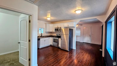 Kitchen featuring white cabinetry, stainless steel appliances, dark countertops, a textured ceiling, and dark wood-type flooring