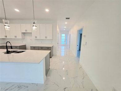 Kitchen with light marble finish floors, pendant lighting, light stone countertops, recessed lighting, and white cabinetry