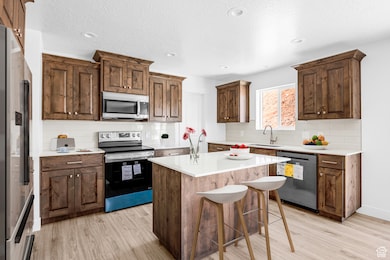 Kitchen with stainless steel appliances, light wood-style floors, light countertops, a kitchen island, and decorative backsplash