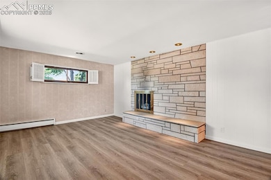 Unfurnished living room featuring wood finished floors, a stone fireplace, and a baseboard radiator