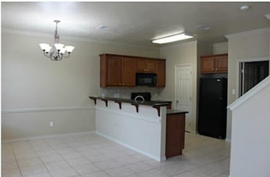Kitchen featuring dark countertops, brown cabinetry, black appliances, a peninsula, and crown molding