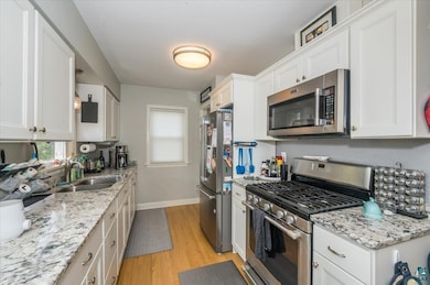 Kitchen featuring appliances with stainless steel finishes, white cabinets, light wood-style floors, and light stone countertops