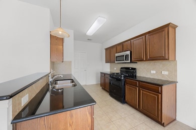 Kitchen with tasteful backsplash, black range with gas cooktop, hanging light fixtures, light tile patterned floors, and stainless steel microwave