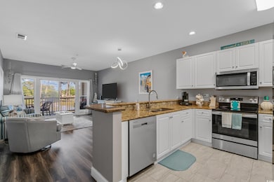 Kitchen featuring white cabinets, appliances with stainless steel finishes, a sink, a peninsula, and open floor plan