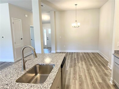Kitchen with light wood-style floors, hanging light fixtures, light stone countertops, a chandelier, and stainless steel dishwasher