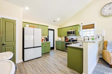 Kitchen with green cabinets, stainless steel appliances, light stone counters, light wood-style flooring, and high vaulted ceiling
