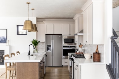 Kitchen featuring a kitchen bar, appliances with stainless steel finishes, white cabinets, and decorative light fixtures