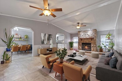 Living room featuring vaulted ceiling, crown molding, ceiling fan, arched walkways, and a stone fireplace